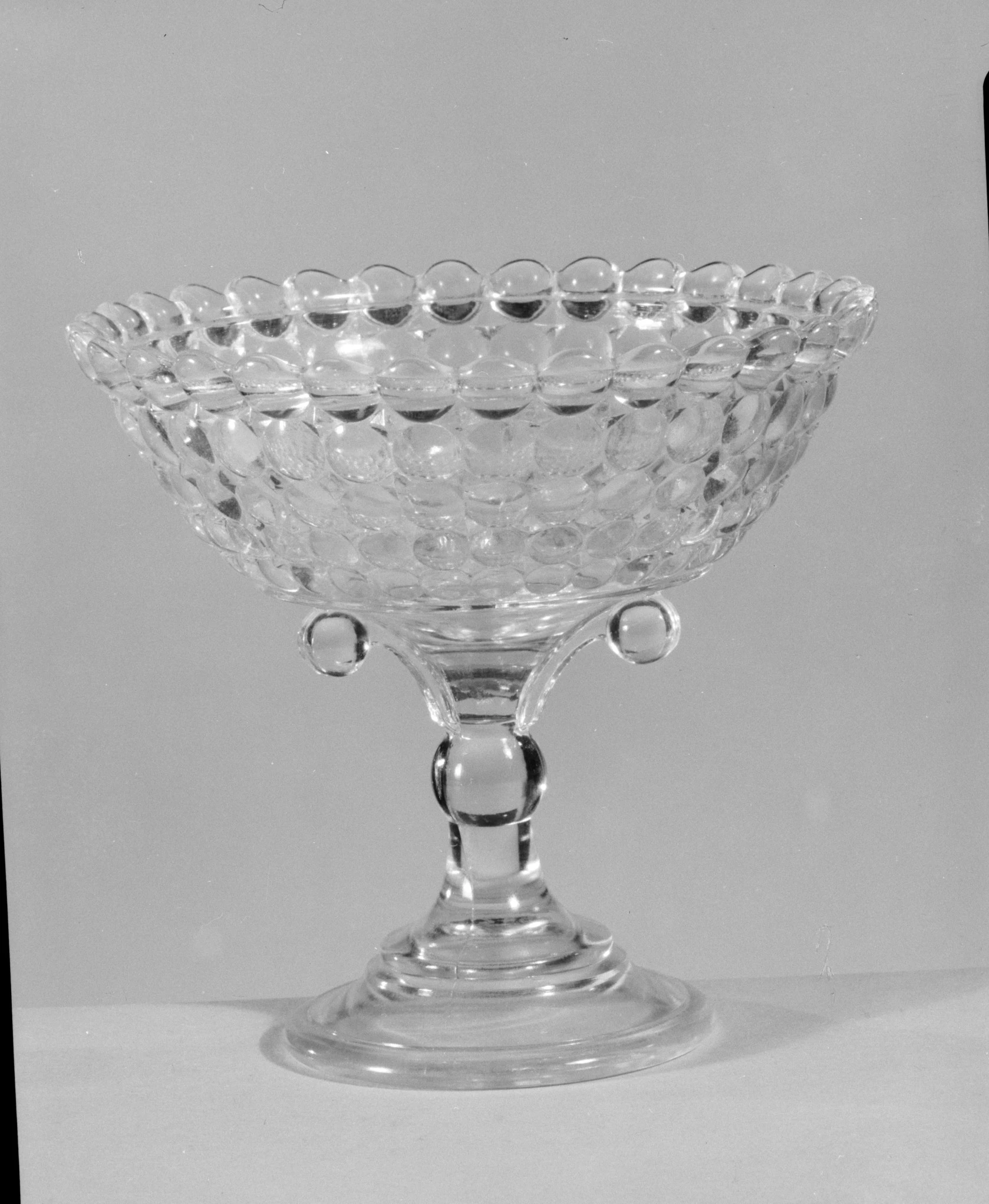 A footed pressed glass compote in the "Thousand Eye" pattern, its bowl covered in a repeating grid of raised round bosses, on a knopped stem and oval foot