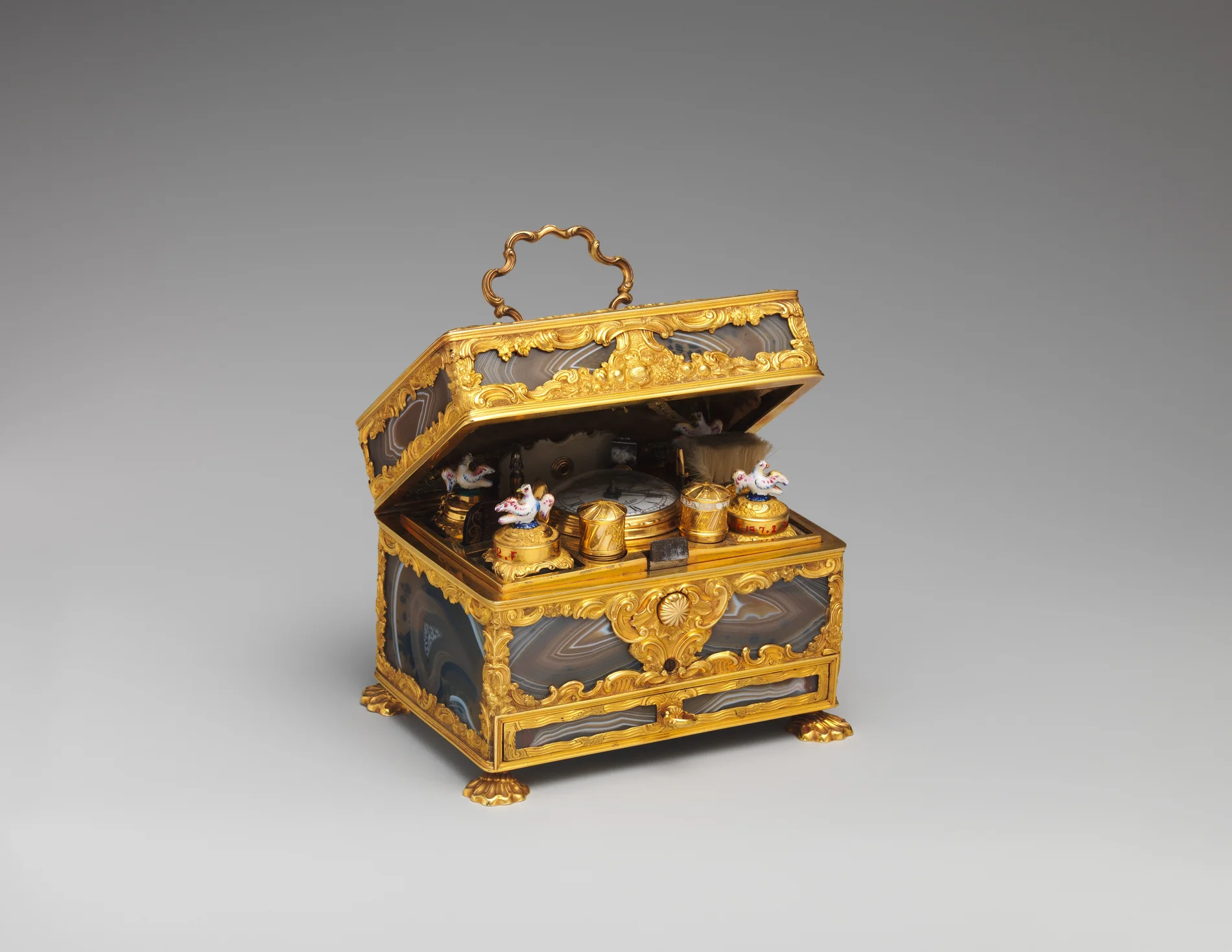 An open gold and banded-agate nécessaire case from the mid-18th century, its lid raised to show a small watch, several enamel boxes, two porcelain birds and other fitted implements inside