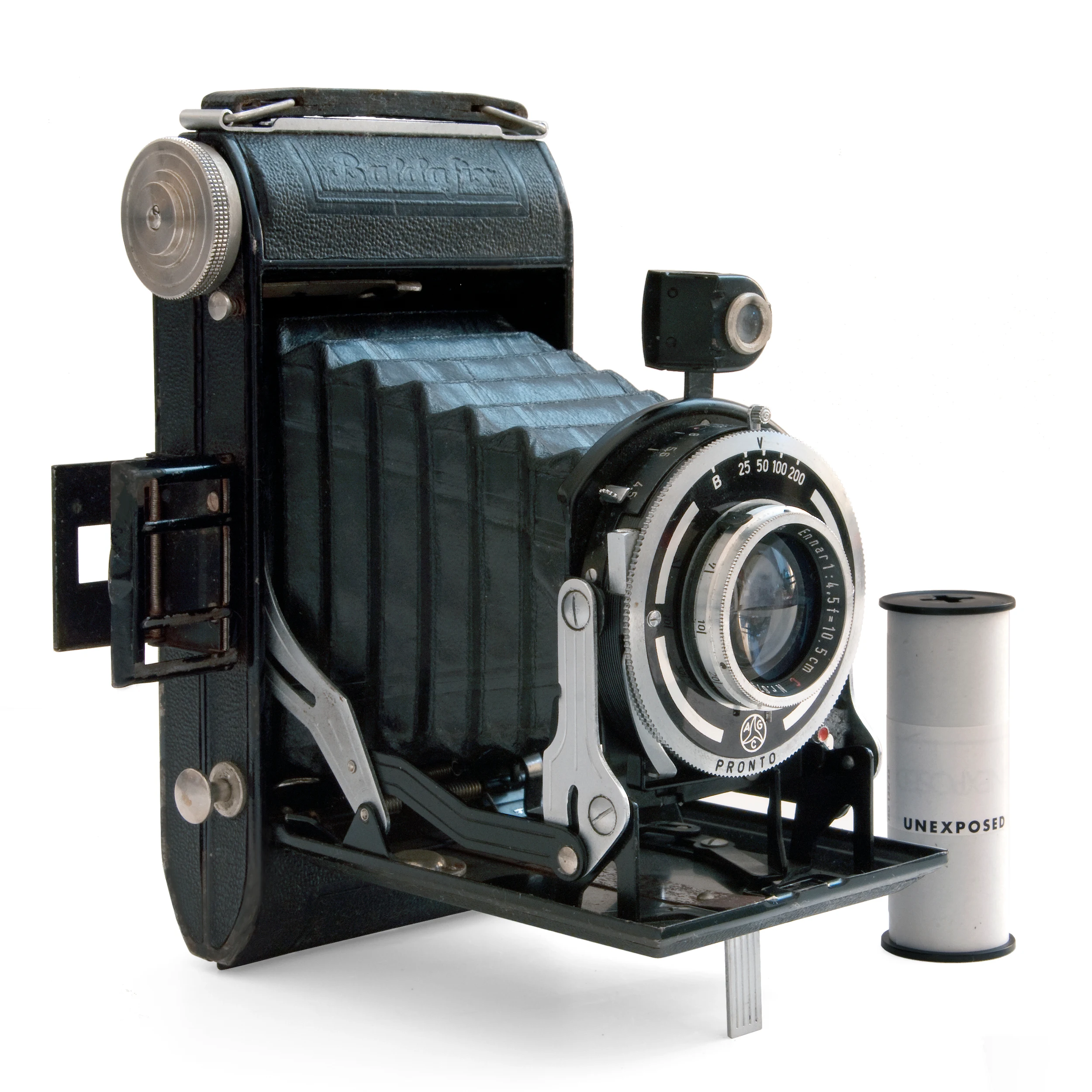 A vintage folding bellows camera photographed against a plain neutral background, with an unexposed roll of film resting beside it