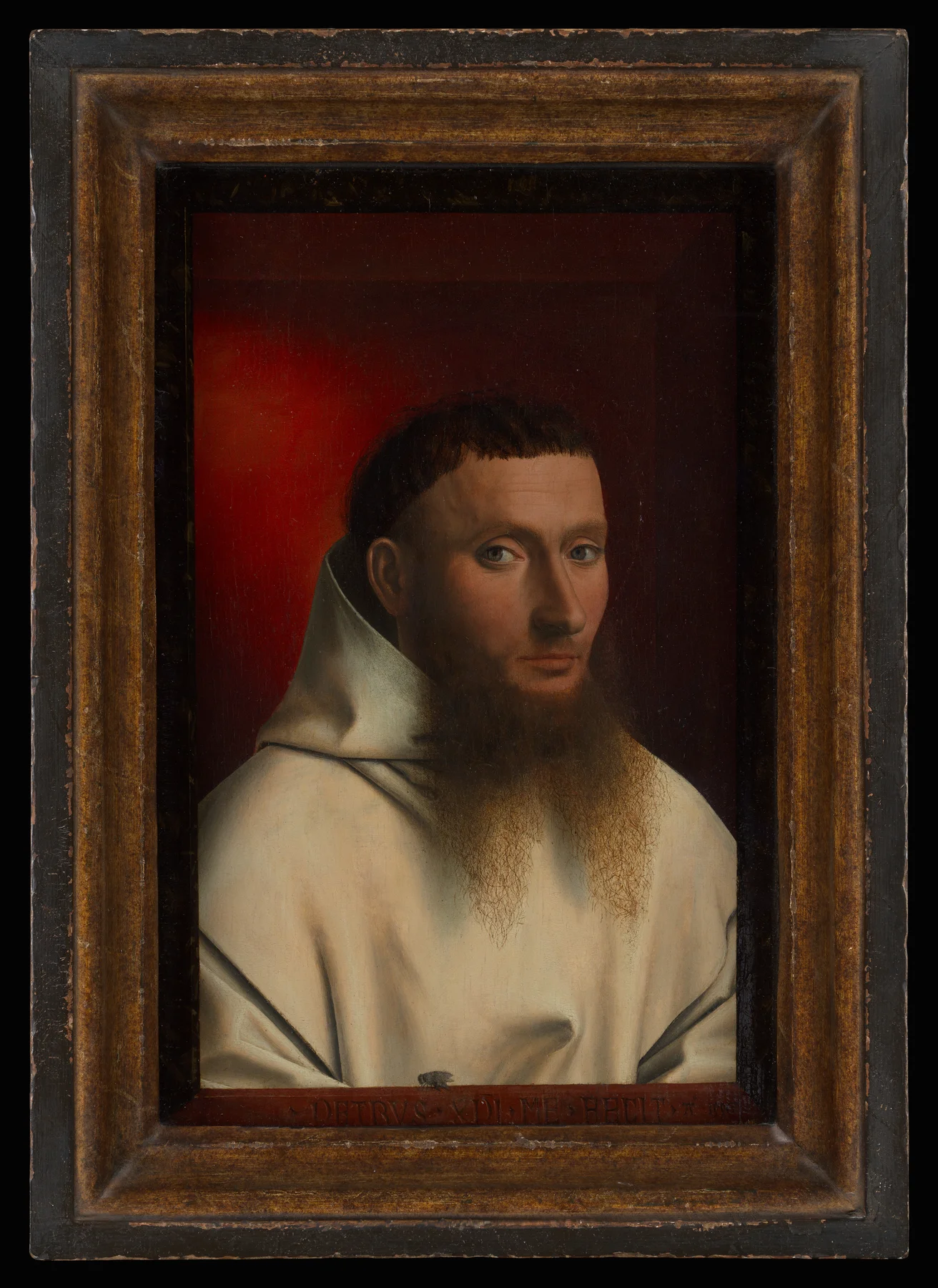 Petrus Christus's 1446 oil portrait of a bearded Carthusian monk in a white habit against a red ground, with a Latin inscription reading "Petrus Christus me fecit" painted along the bottom ledge and a small trompe l'oeil fly resting on the ledge