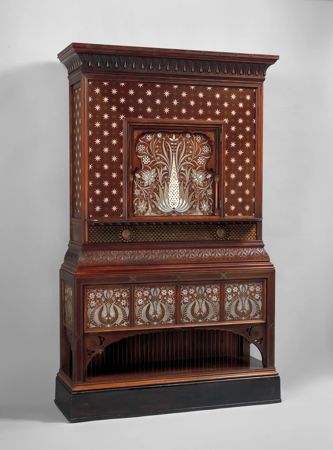 A tall Aesthetic Movement cabinet in dark rosewood, its doors and panels inlaid with hundreds of small mother-of-pearl stars and a large mother-of-pearl flower motif, dated 1884 to 1885