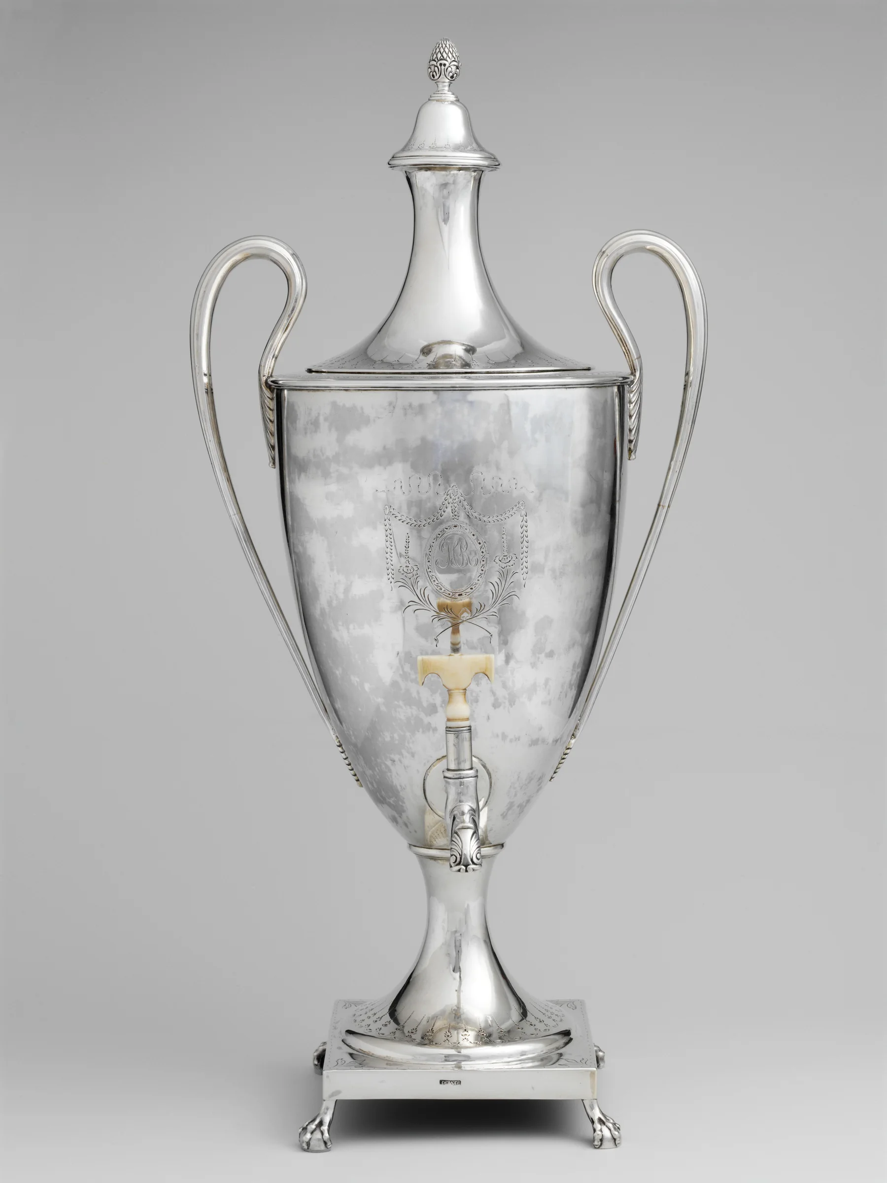 A tall silver tea urn with double scroll handles, a pineapple finial and an ivory spigot handle, made by Paul Revere Jr. in 1791