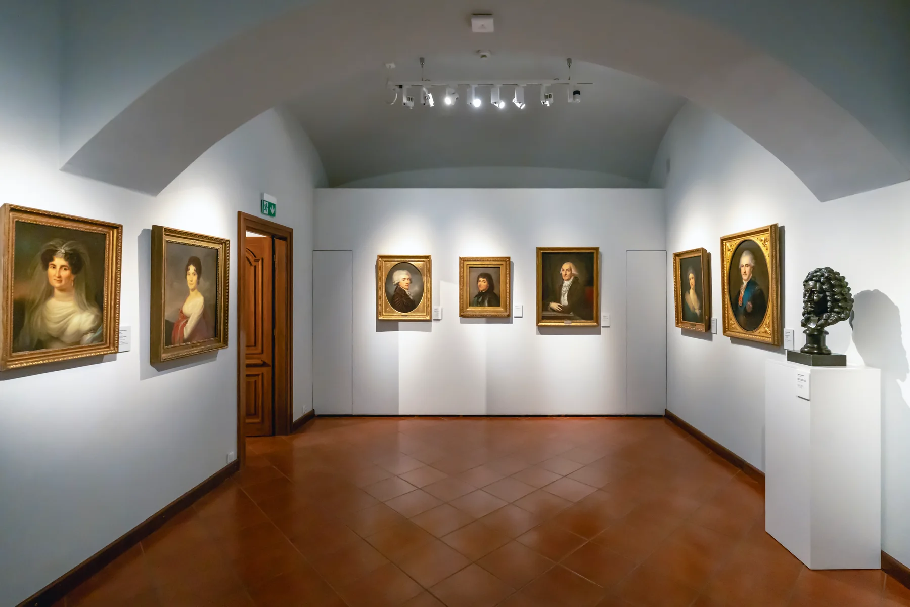 An empty museum gallery room with portrait paintings in gilt frames and a bronze bust on a plinth, used here as a generic representative image and not a photograph of the B.J. Spoke Gallery